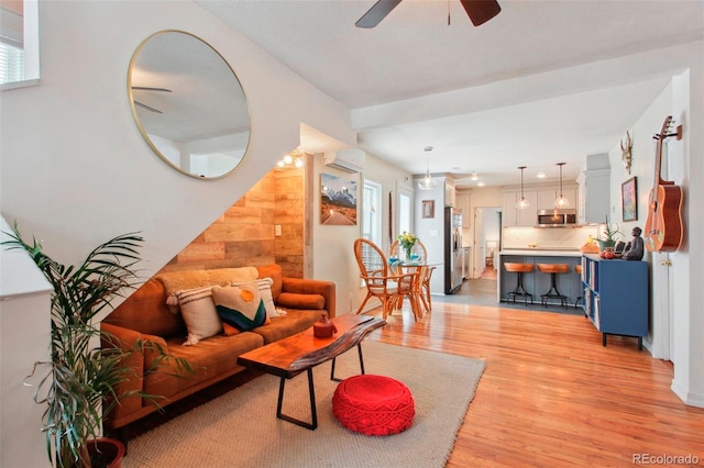 living room with a ceiling fan, an AC wall unit, a healthy amount of sunlight, wood walls, and light wood-type flooring