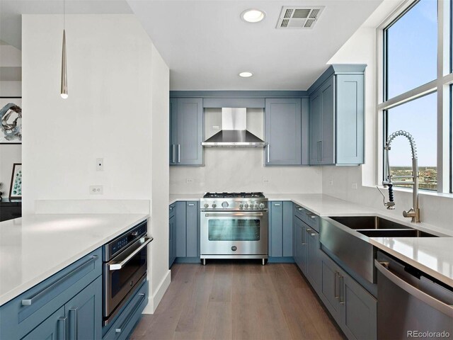 2001 Lincoln St Unit 1822, Denver, CO 80202 - kitchen featuring light countertops, visible vents, wall chimney exhaust hood, appliances with stainless steel finishes, and dark wood-type flooring