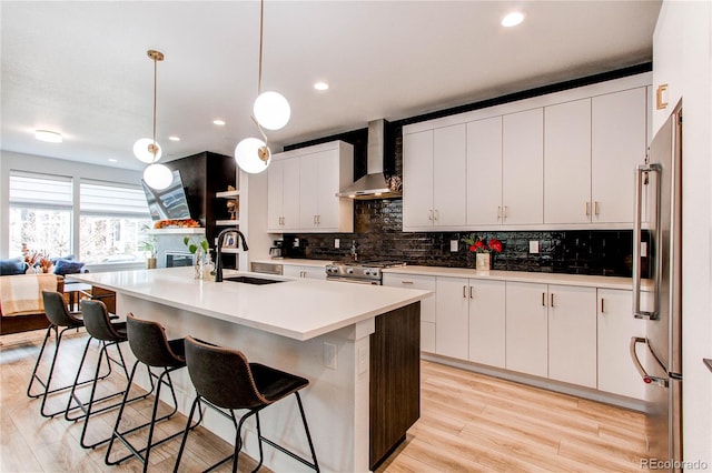 kitchen with a center island with sink, sink, wall chimney exhaust hood, decorative light fixtures, and white cabinetry