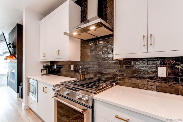 kitchen with wall chimney exhaust hood, stainless steel appliances, tasteful backsplash, light hardwood / wood-style flooring, and white cabinets