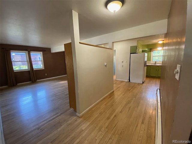 hall featuring a baseboard heating unit, sink, and light wood-type flooring