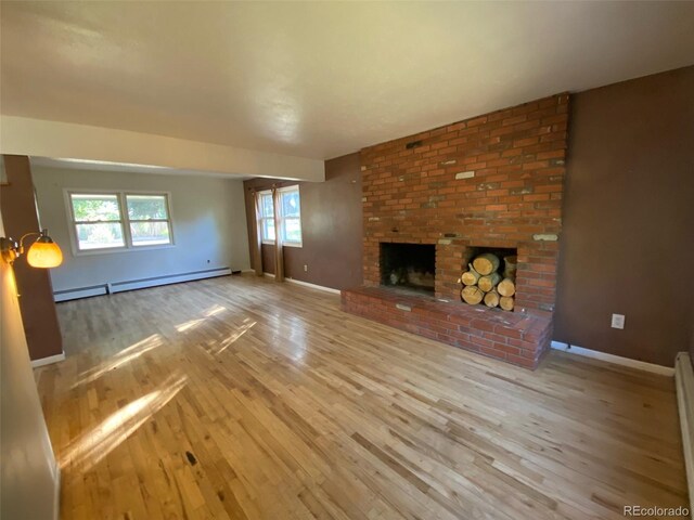 unfurnished living room with light wood-type flooring, baseboard heating, a fireplace, and brick wall