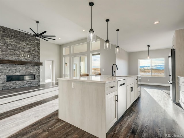 kitchen featuring dark wood-type flooring, sink, a center island with sink, white cabinets, and a stone fireplace