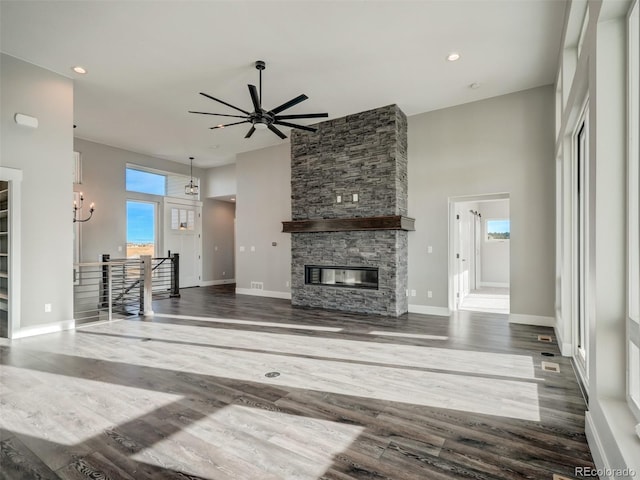 living room with ceiling fan, a stone fireplace, a towering ceiling, and dark wood-type flooring