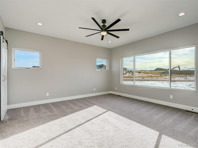 unfurnished room with a barn door, carpet floors, and ceiling fan