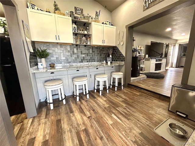 kitchen with wood finished floors, decorative backsplash, a kitchen breakfast bar, vaulted ceiling, and open shelves