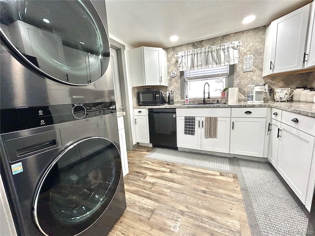 kitchen featuring black appliances, a sink, stacked washer / dryer, light wood-type flooring, and white cabinets