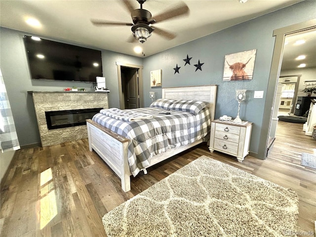 bedroom with wood finished floors, a fireplace, baseboards, and ceiling fan