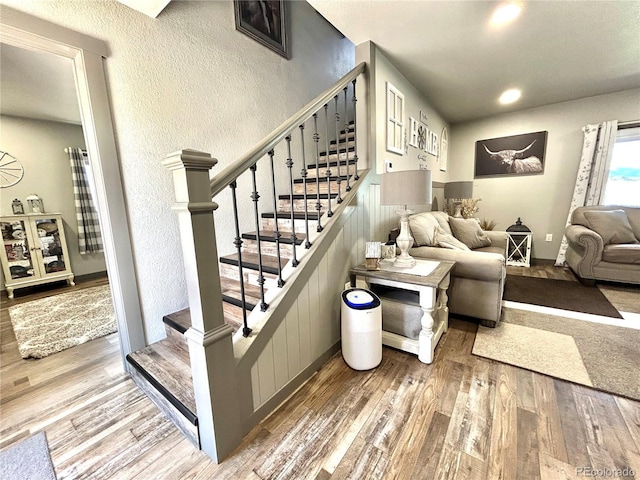 staircase featuring a textured wall, wood finished floors, recessed lighting, and wainscoting