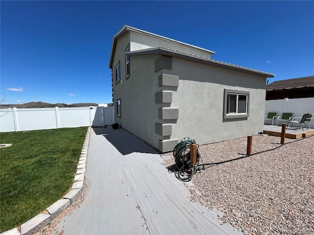 view of property exterior with a wooden deck, stucco siding, a patio area, and a gate
