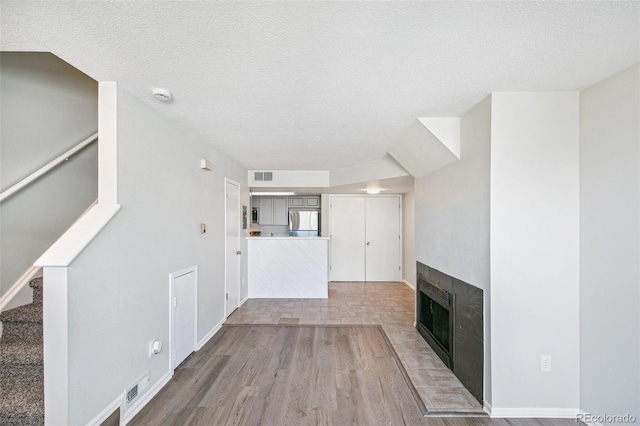 17094 E Tennessee Dr Unit 212, Aurora, CO 80017 - unfurnished living room featuring a textured ceiling, light wood-style flooring, a fireplace, stairs, and baseboards