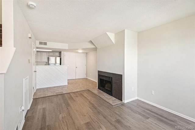 17094 E Tennessee Dr Unit 212, Aurora, CO 80017 - unfurnished living room featuring wood finished floors, a tiled fireplace, baseboards, and a textured ceiling