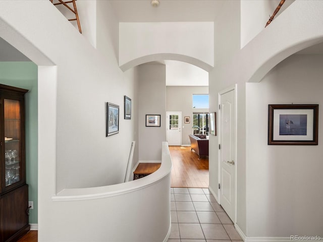 hallway featuring tile patterned floors, a high ceiling, and baseboards