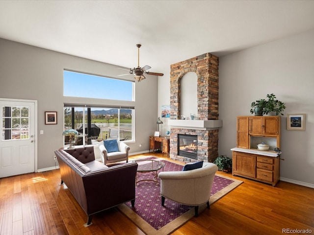 living room with baseboards, a ceiling fan, light wood finished floors, and a fireplace