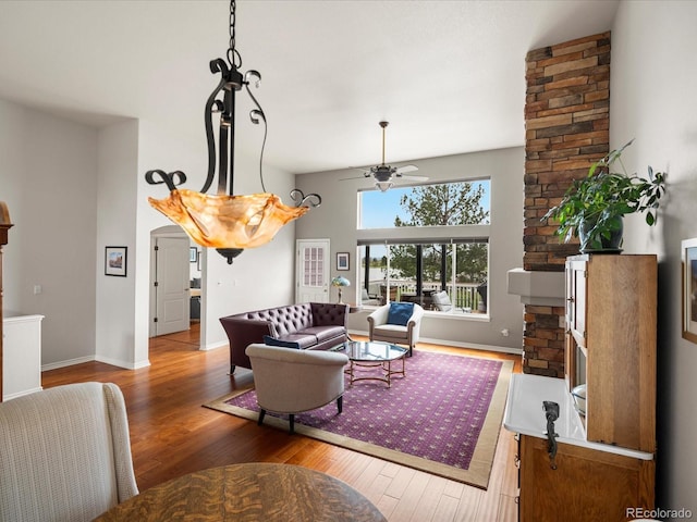 living area with baseboards, ceiling fan, a stone fireplace, and wood finished floors