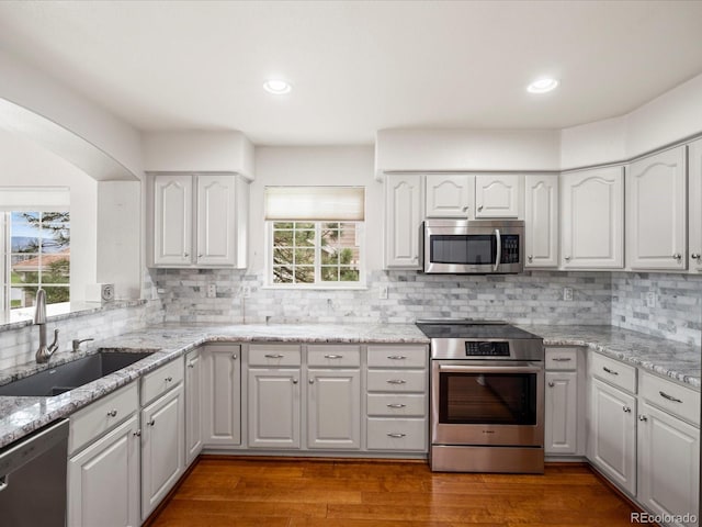 kitchen with decorative backsplash, light stone countertops, a sink, white cabinets, and stainless steel appliances