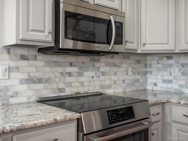 kitchen with decorative backsplash, white cabinets, light stone countertops, and stainless steel appliances