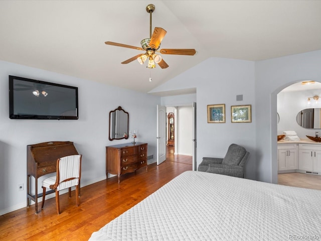 bedroom with connected bathroom, light wood finished floors, visible vents, arched walkways, and vaulted ceiling