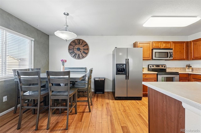4705 Andes St, Denver, CO 80249 - kitchen featuring stainless steel appliances, brown cabinets, light countertops, light wood-style floors, and hanging light fixtures