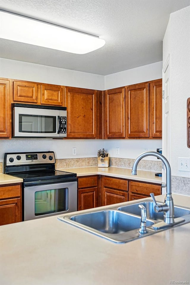 4705 Andes St, Denver, CO 80249 - kitchen featuring appliances with stainless steel finishes, a sink, light countertops, brown cabinets, and a textured ceiling