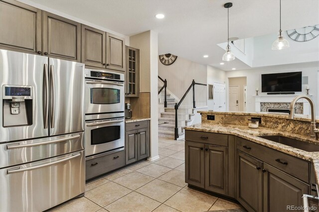 kitchen featuring appliances with stainless steel finishes, a sink, light stone countertops, light tile patterned floors, and glass insert cabinets