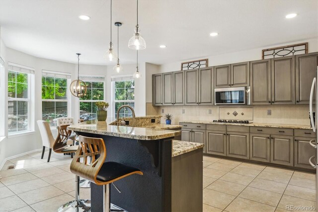 kitchen with stainless steel microwave, light tile patterned floors, gas stovetop, backsplash, and a breakfast bar