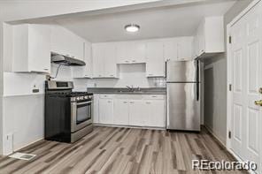 kitchen featuring white cabinets, light hardwood / wood-style flooring, sink, range hood, and stainless steel appliances