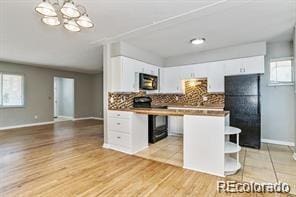 kitchen featuring a wealth of natural light, black appliances, light hardwood / wood-style flooring, and white cabinets