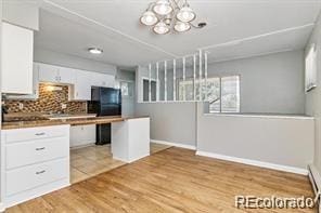 kitchen featuring decorative backsplash, light hardwood / wood-style flooring, black refrigerator, a chandelier, and white cabinetry