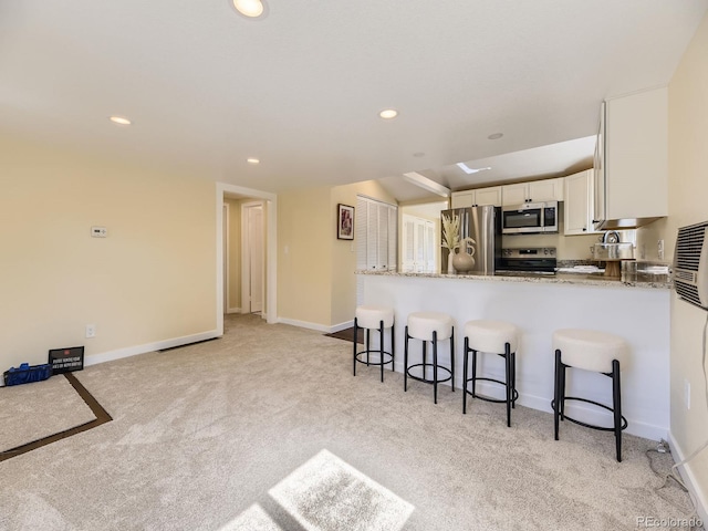 kitchen with kitchen peninsula, a kitchen bar, light colored carpet, appliances with stainless steel finishes, and light stone countertops