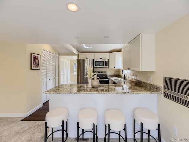 kitchen with white cabinetry, light stone counters, kitchen peninsula, stainless steel appliances, and carpet flooring