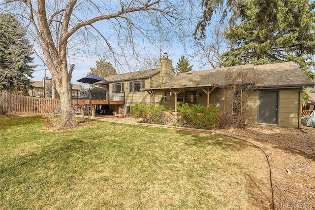 rear view of house featuring a chimney, a lawn, a wooden deck, fence, and a shingled roof