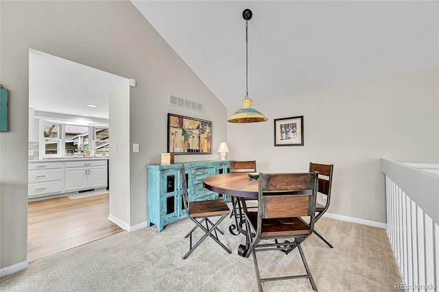 dining room with high vaulted ceiling, visible vents, light colored carpet, and baseboards