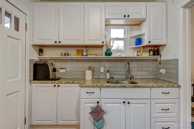 kitchen with decorative backsplash, white cabinetry, sink, and light stone counters