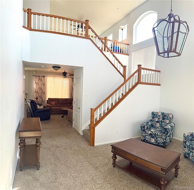 stairs with carpet floors, ceiling fan, a towering ceiling, and baseboards