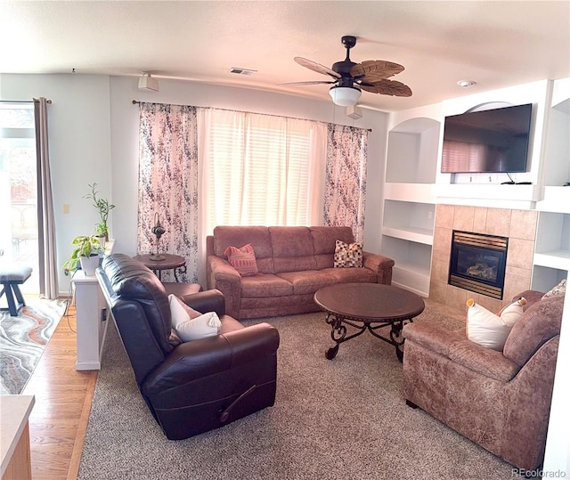 living room with built in shelves, visible vents, a ceiling fan, light wood-type flooring, and a tile fireplace