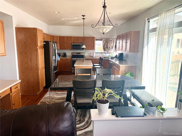 kitchen featuring stainless steel appliances, hanging light fixtures, light countertops, and brown cabinets