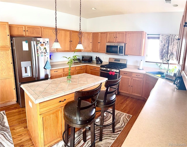 kitchen featuring a kitchen island, wood finished floors, hanging light fixtures, stainless steel appliances, and a sink