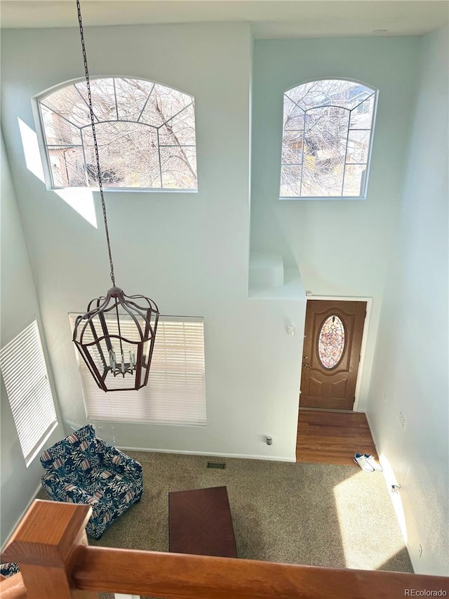 carpeted entrance foyer featuring visible vents, a towering ceiling, and a notable chandelier