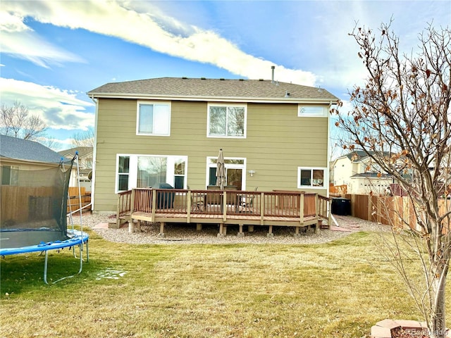 rear view of house with a trampoline, a fenced backyard, a yard, and a wooden deck