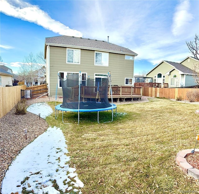 back of house featuring a deck, a trampoline, a fenced backyard, and a lawn