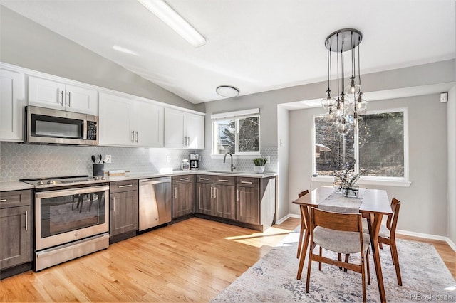 kitchen featuring a sink, stainless steel appliances, white cabinets, light countertops, and lofted ceiling