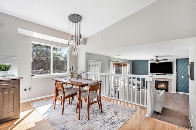 dining room with baseboards, ceiling fan with notable chandelier, light wood-style flooring, and a tile fireplace