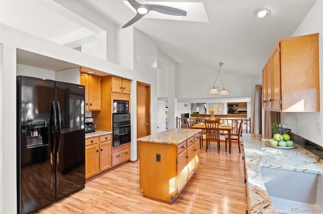 kitchen featuring black appliances, a center island, ceiling fan, hanging light fixtures, and light stone counters