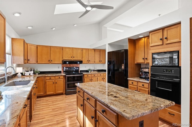 kitchen with a center island, black appliances, sink, a skylight, and light stone countertops