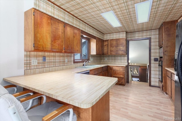 kitchen with a breakfast bar area, a peninsula, a sink, light countertops, and brown cabinetry