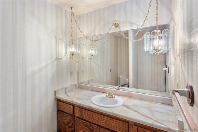 bathroom with toilet, wallpapered walls, an inviting chandelier, and vanity