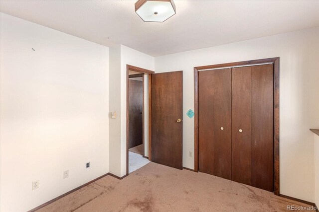 unfurnished bedroom with light carpet, baseboards, and a closet