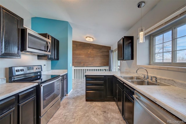 kitchen featuring vaulted ceiling, wood walls, sink, hanging light fixtures, and stainless steel appliances