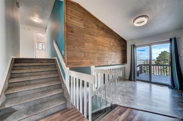 stairs featuring hardwood / wood-style floors, vaulted ceiling, a textured ceiling, and wood walls